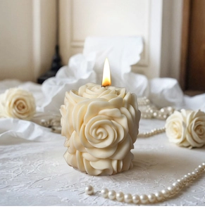 Dettaglio candela a colonna rosa bianco crema con trame floreali 3D e fiamma accesa