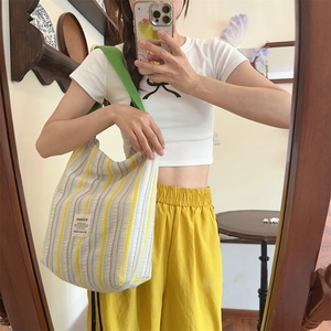 Détail du sac cabas en toile à rayures jaunes avec bandoulière verte et étiquette