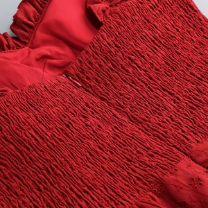 Macro detail of red off-shoulder dress featuring intricate eyelet embroidery and smocked fabric