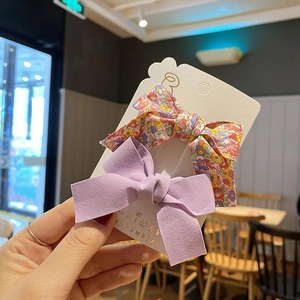 Detail of floral and purple fabric bow hair clips for kids on a white card