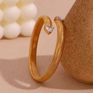 Detailed macro shot of a gold spiral bangle with heart-shaped zircon stones on a stone