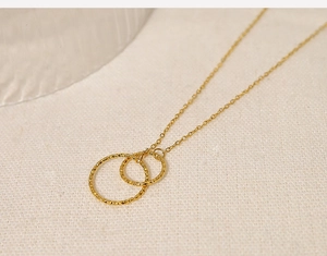 Detailed close-up of double-loop hammered gold titanium necklace on fabric