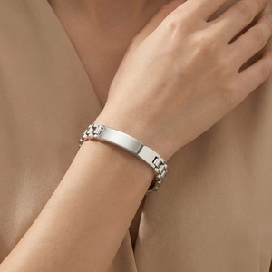 Detailweergave van een zilveren roestvrijstalen armband met ID-plaatje en horlogeband-schakels om pols