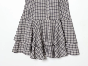 Detail of layered ruffle hem with plaid pattern and decorative buttons on a grey dress