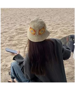 Detail of hand-woven straw bucket hat with colorful sunflower pattern on sandy beach