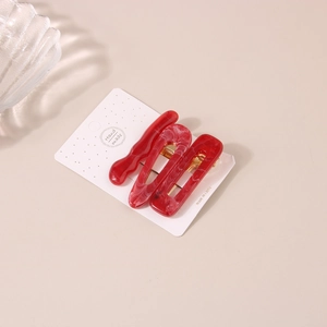 Gros plan de trois pinces à cheveux à motif marbre rouge et blanc sur support cartonné