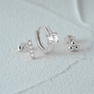 Macro view of a 3-piece silver earring set with zircons on white stone background