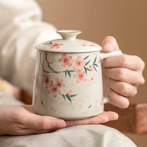Hand-painted peach blossom ceramic mug with lid, stylish Chinese floral tea cup held in hands