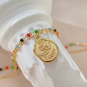 Détail d'un collier vintage doré avec pendentif rose et perles en émail multicolores