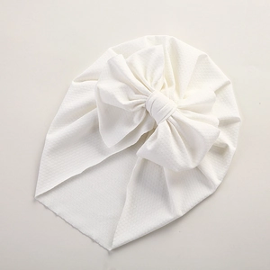 Detailed view of white baby turban featuring textured fabric and a large bow decoration