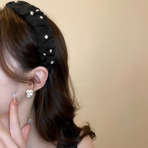 Detail of a black pleated headband with rhinestones and matching gold pearl earrings