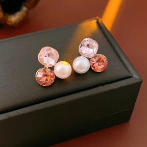 Close-up of elegant triangle stud earrings with pink crystal and white pearl on black box