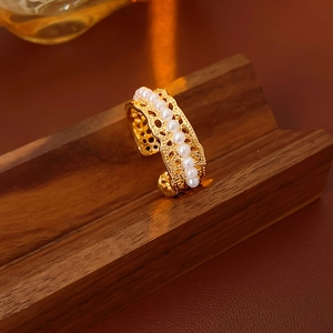 Detail of gold-plated hollow lace ring with elegant pearls on dark wooden stand