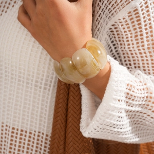 Close-up of wide marble resin bangle with amber tones worn with knitwear
