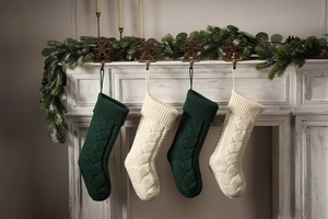 Set of four knitted Christmas stockings in green and off-white hanging on a fireplace