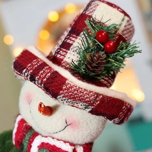Detail showing the plaid plush hat with pine needles and berries on a Christmas snowman doll