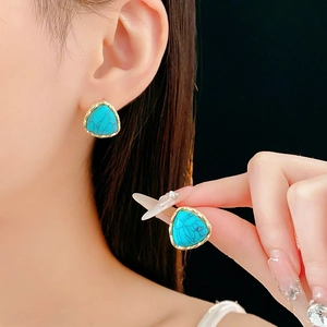 Macro detail of turquoise triangle earring with gold frame on model ear and hand