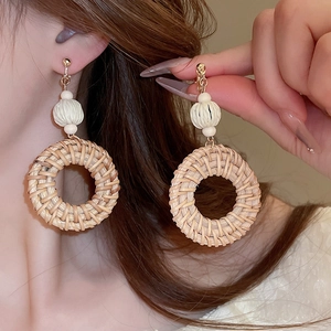 Close-up of model wearing round beige rattan drop earrings for a beach vacation style