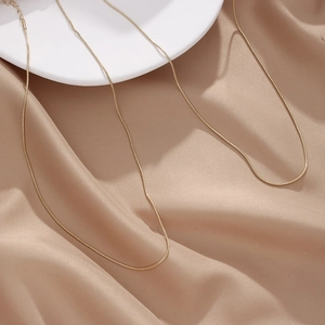 Detailed macro view of a gold snake bone chain necklace on champagne satin and ceramic