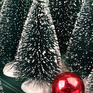 Close-up of miniature green Christmas trees with white snow flocking and red ornament