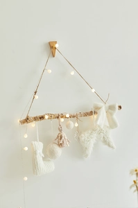 Detail of knit Christmas wall hanging with wood branch, tassels and warm LED lights