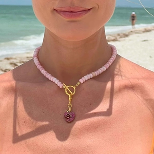 Pink beaded necklace with strawberry pendant and gold OT clasp worn on a sunny beach