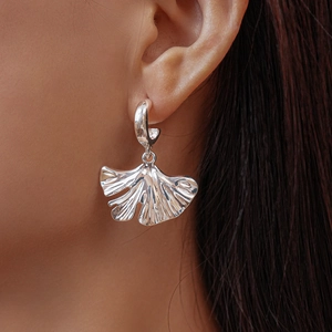 Detailed close-up of a silver ginkgo leaf earring with textured folds on a female model