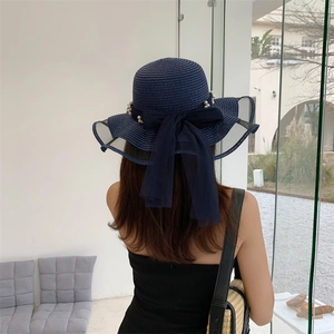 Close-up of dark blue straw sun hat featuring a sheer bow and elegant white pearls