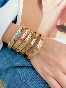 Bracelets dorés empilés avec zircons colorés portés sur du denim pour un style tendance