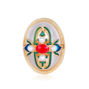 Macro shot of oval gold alloy brooch with red gem, green enamel, and small white pearls