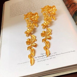 Close-up of golden flower leaf tassel earrings on a vintage book page backdrop