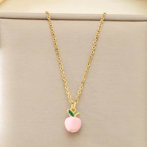 Detail of a gold chain necklace with a pink enamel apple pendant and green leaf