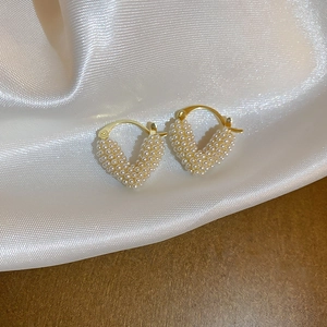 Detailed macro view of heart-shaped gold earrings with paved white pearls on white silk