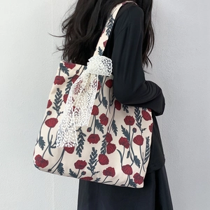 Detail view of canvas tote bag with red poppy print and white lace bow accessory