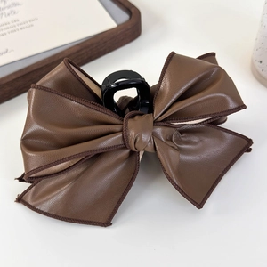 Detailed view of a large brown faux leather bow hair claw clip with visible stitching