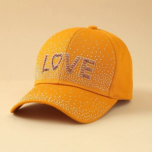 Detailed view of stylish orange baseball cap featuring shimmering rhinestone LOVE lettering
