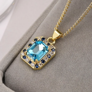 Macro detail of sky blue square zircon pendant with gold chain in a velvet jewelry box