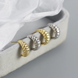 Detailed view of gold and silver ribbed croissant hoop earrings on a soft jewelry box