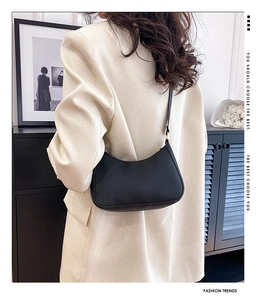 Detailed view of a sleek black leather crescent shoulder bag worn on a model's arm