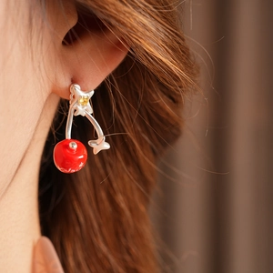 Close-up of a silver cherry earring with zircon star and red bead on a model ear