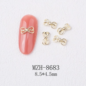 Macro view of 8.5x4.5mm golden alloy bow nail charms on a soft pink manicure base