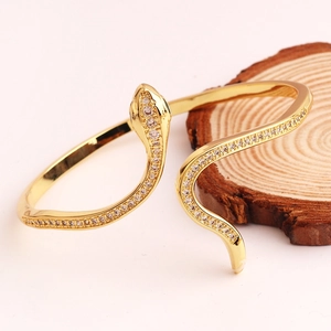 Detail of gold snake bracelet with white crystal pavé setting on a wooden stand