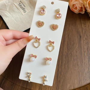 Close-up of pearl earrings set with pink rhinestones, hearts and bows on display card