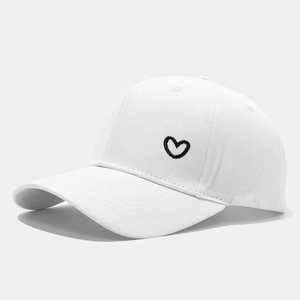 White cotton baseball cap with black heart embroidery on a neutral gray background