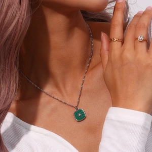Detail of green shell pendant necklace with gold chain rings on a female model