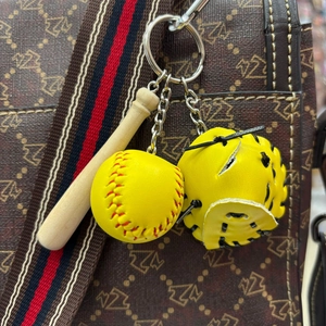 Close-up of mini baseball keychain with wooden bat and yellow glove on a bag strap