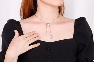 Detail of silver heart-shaped slide clasp and coin pendants on a layered Y-necklace