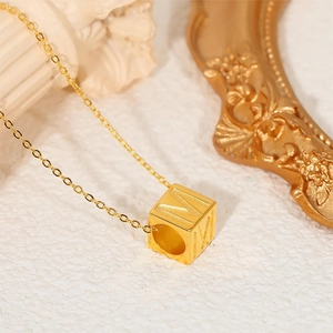 14K gold plated cube necklace with engraved letter M on a white stone pedestal