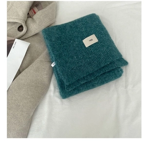 Detailed close-up of dark cyan thick knit wool scarf with minimalist egg brand patch