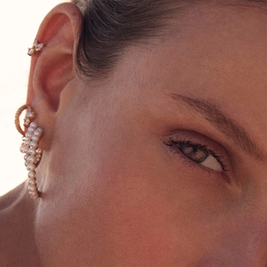 Close-up of pearl curved earrings and crystal clover ear stud on a model's ear